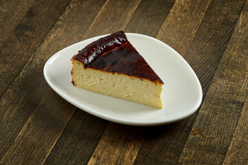 Delicious homemade pastry - a slice of Basque cheesecake, served on a white plate on a wooden background.