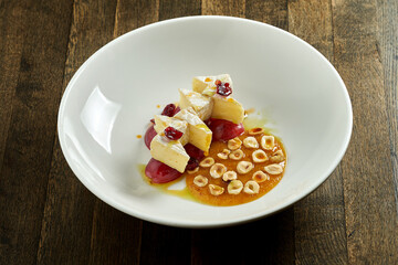 Delicious appetizer - baked brie cheese with hazelnuts, grapes and caramel honey sauce, served in a white plate on a wooden background. Cheese fondue