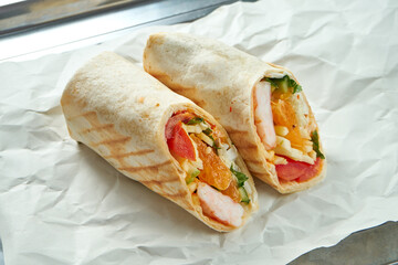 Appetizing doner roll with vegetables, sauce and shrimp in pita bread, served on paper on a light background. Traditional street food - shawarma