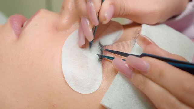 The girl is lashed with blue tweezers in the salon for non-lashing