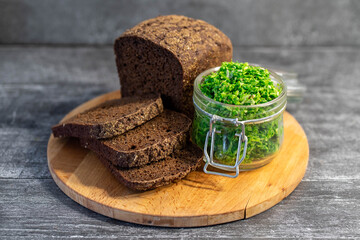 Wild leek pesto with olive oil in a glass jar on a wooden table with bread. Useful properties of wild garlic. Fresh bear onion leaves.
