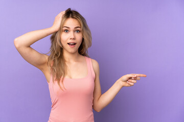 Fototapeta premium Teenager Russian girl isolated on purple background surprised and pointing finger to the side