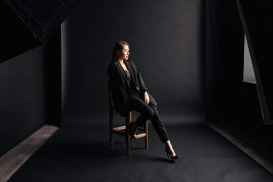 beautiful caucasian woman sitting on a chair in a photo studio in a black formal suit