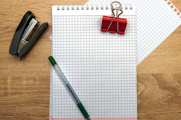 two open notepads a fountain pen a stapler and a stationery clip on the table