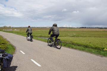 Dutch pasture landscape. Cyclists, who ride in the spring on a road along the meadows. Cloudy sky....