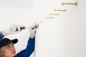 a worker screws fasteners for hanging kitchen cabinets to the white wall with self-tapping screws,...