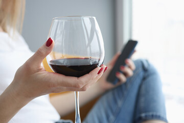 Female hand holds glass of wine and smartphone