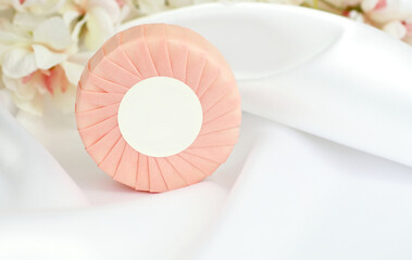 Fototapeta na wymiar Round solid soap bar in pink paper package on white silk background