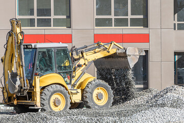 Yellow excavator pours gray rubble for road repair in the city in sunny day