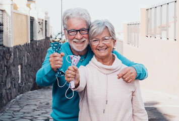 Beautiful senior couple already vaccinated against coronavirus infection - smiles happily outdoors taking off their protective masks