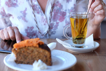 Close-up on woman's hand in coffee shop, enjoying an herbal tea and a slice of carrot cake