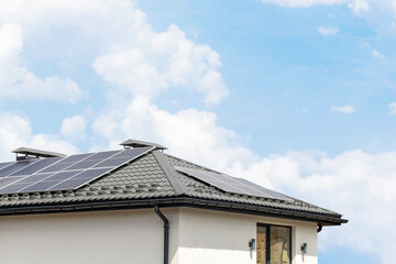 Solar panels on the roof of the house. Renewable solar energy. Blue sky and white clouds. Copy space for text