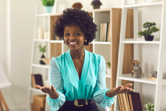 Office people lifestyle emotion, internet business training webinar concept. Happy young African American woman with curly hairstyle smiling stretch hands to camera talk to invisible online audience