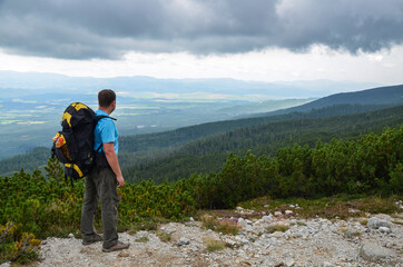 Fototapeta premium Hiker with backpack standing on top of a mountain and enjoying the view of the valley. Concept motivation and goal achievement