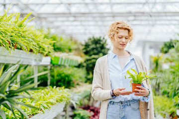 Portrait of german woman chooses flowers in flower shop or greenhouse around of green plants.