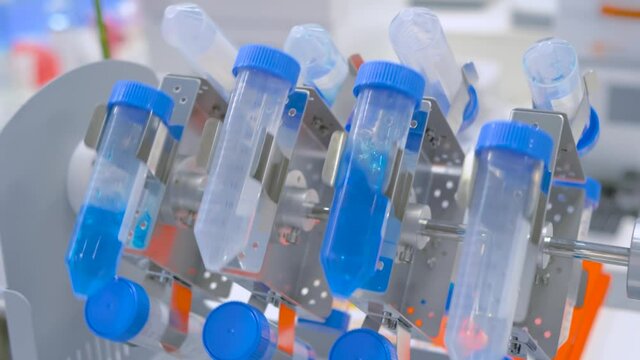 Slow motion: digital tube rotisserie rotator for effective mixing blue biological samples at pharmacy factory, medical exhibition: close up. Chemistry, pharmaceutical, laboratory equipment concept