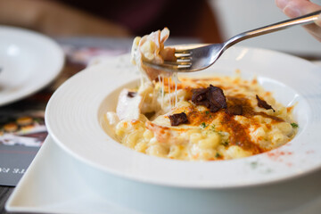 Cheese stretched with fork is being dipped in macaroni cheese with bacon paprika chilli is topping.