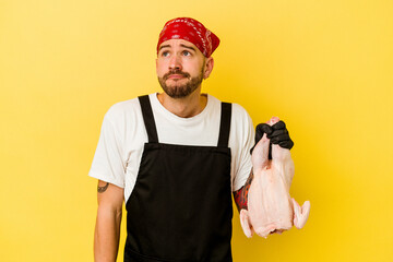 Young tattooed batcher caucasian man holding a chicken isolated on yellow background dreaming of achieving goals and purposes