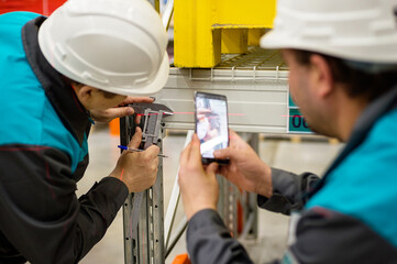 Two male engineers in helmets carry out tests, record it on phone