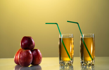 Apple juice in a glass with drinking straws. Beautiful sunset yellow background. Red apples