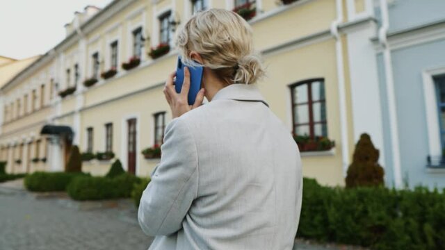 A back view at blond-haired businesswoman walking and talking on the smartphone