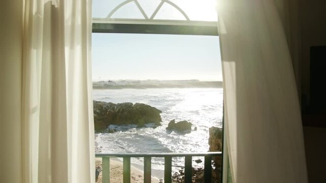 Baleal, Portugal. Beachfront window with a sunset in the background. Beautiful room interior with sandy beach and rocks in front. High quality 4k footage