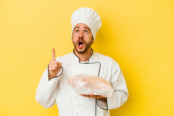 Young caucasian chef man holding chicken isolated on yellow background pointing upside with opened mouth.
