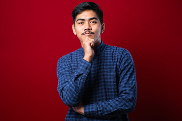 Handsome asian man with mustache wearing casual shirt over red background looking confident at the camera
