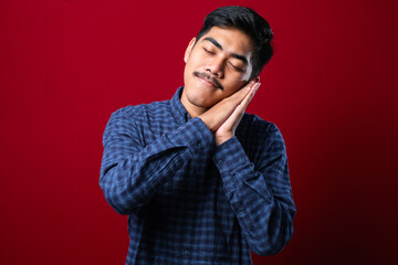 Fototapeta premium Asian handsome man wearing shirt sleeping tired dreaming and posing with hands together while smiling with closed eyes