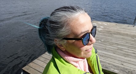 Photo of a woman's face with ponytail hair, sunglasses, a pink sweatshirt and a light green jacket