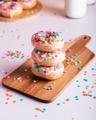 Stack of freshly made home cooked donuts with icing and sprinkles and milk bottle and glass in background