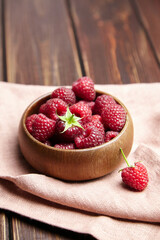 Fresh raspberries in wooden bowl on brown table. Red ripe raspberries, sweet berries