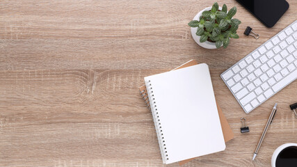 Top view wooden workspace office desk with computer and office supplies. Flat lay work table with blank notebook, keyboard, green leaf, pen and coffee cup. Copy space for your advertising content.