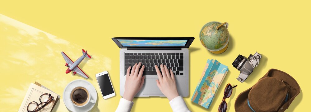 ノートパソコンをタイピングする手。海外旅行にまつわるアイテム。旅行の計画をたてているところ。もしくは、インターネットで旅行の疑似体験をしているところ。真上からのアングル