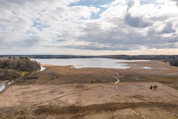 Photo from the drone. a narrow river flows into the bay. Finland. Scandinavian nature in early spring. Yellow grass in the fields. There are a lot of reeds in the bay.