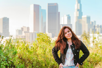 Young beautiful brunette woman stands with a view of Downtown skyscrapers in Los Angeles