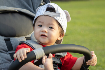 Happy and cute Asian Chinese baby boy sitting on stroller at park during evening