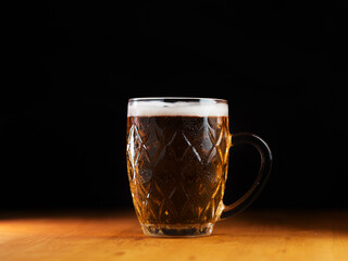 Glass of light beer on a wooden table, black background