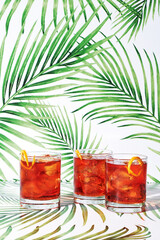Three Red Negroni Cocktails on Green Tropical Background
