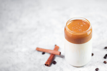 Dalgona coffee. Whipped Korean trend drink with coffee and milk. Creative glass, concrete white table, coffee beans and cinnamon stick