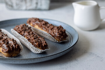 Three eclairs on blue plate and creamer on grey background