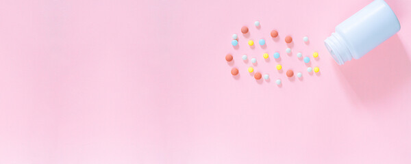 Multicolored tablets, pills, capsules in plastic bottle on pink background, copy space. Heap of assorted various medicine tablets and pills, vitamin and nutritional supplements concept.