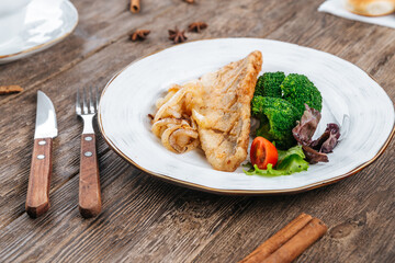 Fried fish fillet with fresh vegetables on a wooden table
