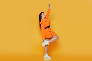 Beautiful girl on a yellow background. A brunette in an orange dress and long hair is posing, dancing, laughing, having fun. Woman warm summer photo in studio. Joy and emotion