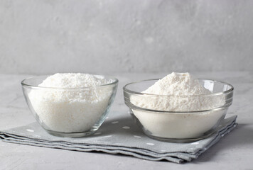 Vegan coconut products: coconut flakes and flour in transparent bowls on a gray background.