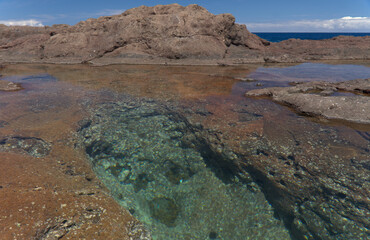 Fototapeta na wymiar Gran Canaria, calm natural seawater pools in under the steep cliffs of the north coast, separated from the ocean by volcanic rock, Punta de Galdar area 