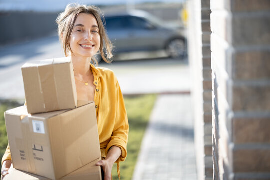 Young happy woman carries home a parcels with goods purchased online, knocking on the door. Concept of online shopping and delivery. Looking at camera.