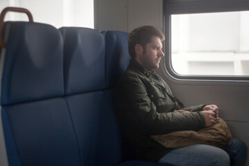 a man with a backpack sits on a seat in an electric train with a ticket in his hands