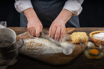 Women's hands, flour and dough. A woman in an apron cooking dough for homemade baking, a rustic home cozy atmosphere, a dark background with unusual lighting.