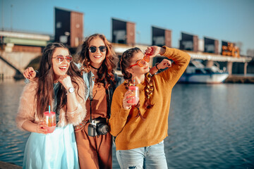 Three girls near the river against the sky having fun. Fashion girls in sunglasses. Jump, rejoice,...